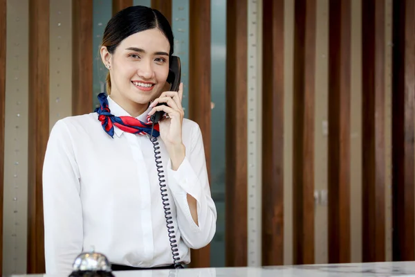 Beautiful smiling Asian female receptionist talking to customer on telephone at reception counter desk hotel, female staff helping guest for booking the hotel on holiday vacation.