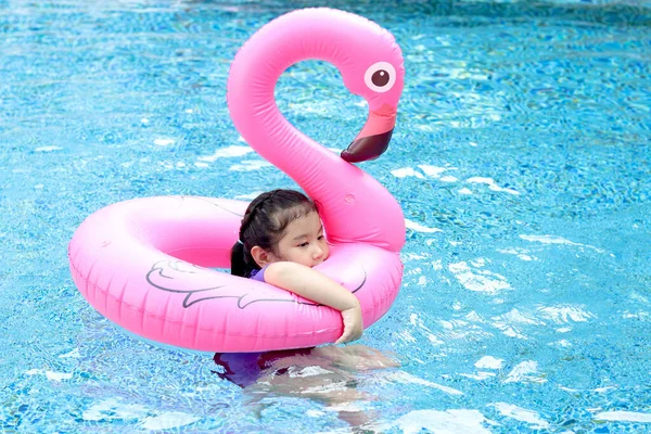 かわいいアジアの少女は青い水でピンクのフラミンゴのプラスチックのおもちゃと泳いで 子供は晴れた日にプールで膨脹可能なチューブで遊んで 夏休みの休日の週末に楽しんでいます — ストック写真