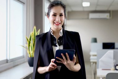 Tablet tutan mutlu gülümseyen Asyalı kadın memurun portresi ofis binasının içinde duran kameraya bakıyor iş yerinde çalışan kendine güvenen modern moda kadın iş kadını..