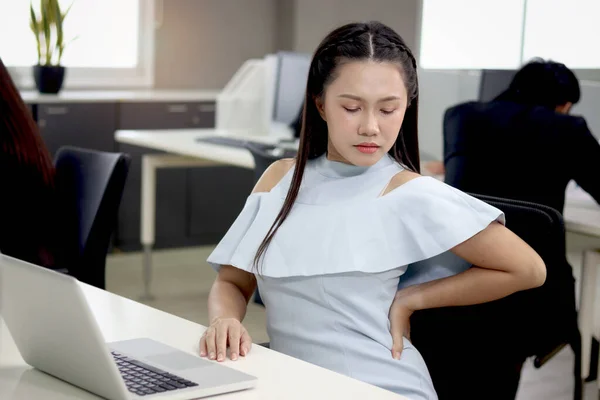Tired beautiful Asian woman officer relieve physical tension during take break from work at office, exhausted female feels pain in back, office syndrome, need resting and stretching body at workplace.