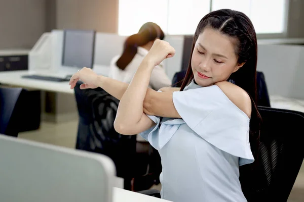 Tired beautiful Asian woman officer relieve physical tension after work hard during take break from work at office desk, exhausted female worker feels sleepy, resting and stretching body at workplace.