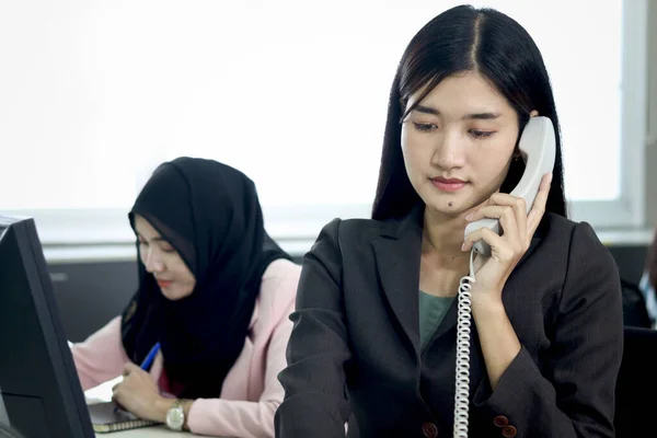 Серьёзная Красивая Азиатская Женщина Оператор Разговаривает Клиентом Стационарному Телефону Столом — стоковое фото