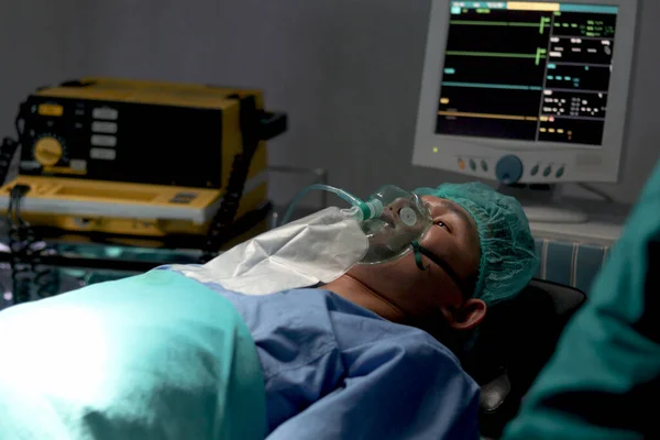 Patient with anesthesia mask or breathing oxygen respiratory equipment lying on operating bed. Patient be prepared for medical treatment by surgeon doctor at operating room in hospital.