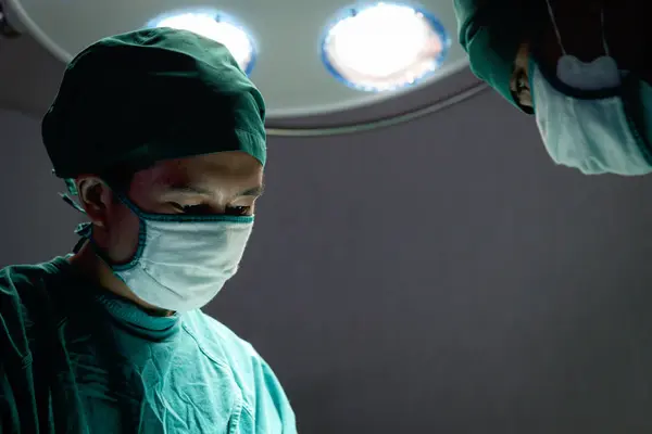 プロの外科医が明るい光の下に立って 病院の手術室で手術を行うために外科機器を使用しています 手術チームが手術患者 ヘルスケア 医療を担当 — ストック写真