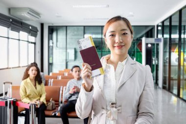 Mutlu gülümseyen güzel Asyalı kadın yolcu havaalanı terminalinde yolcu geçmişi bulanık seyahat, tatil tatili ya da iş seyahati için bekleyen yolcu geçmişi ile pasaport gösteriyor.