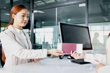 Güzel Asyalı kadın gezgin, havaalanı terminalindeki bilgileri kontrol etmesi, tatil veya iş seyahatinde seyahat etmesi için yolcu hizmet acentesine pasaport verir..