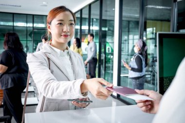 Güzel Asyalı kadın gezgin, havaalanı terminalindeki bilgileri kontrol etmesi, tatil veya iş seyahatinde seyahat etmesi için yolcu hizmet acentesine pasaport verir..