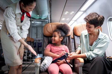 Dost canlısı hostes uçağa binen çocuğa, uçuş görevlisine, kıvırcık saçlı Afrikalı kıza uçak koltuğunda otururken emniyet kemeri takmasını, uçakla seyahat eden çocuğa, havayolu taşımacılığı öğretin.
