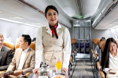 Güzel Asyalı kabin görevlisi kadın hostesi uçaktaki yolculara yiyecek ve içecek servisi yapıyor, uçuş görevlileri servis için koridorda el arabası, havayolu hizmeti ve ulaşım hizmeti veriyor..