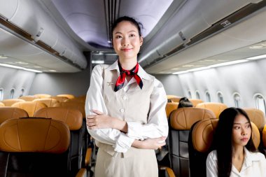 Güzel Asyalı kabin görevlisi kadın hostesinin portresi. Uçakta kollarını kavuşturmuş duruyor. Kadın uçuş görevlisi uçak, havayolu servis taşımacılığında çalışıyor..