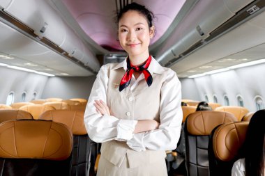 Güzel Asyalı kabin görevlisi kadın hostesinin portresi. Uçakta kollarını kavuşturmuş duruyor. Kadın uçuş görevlisi uçak, havayolu servis taşımacılığında çalışıyor..