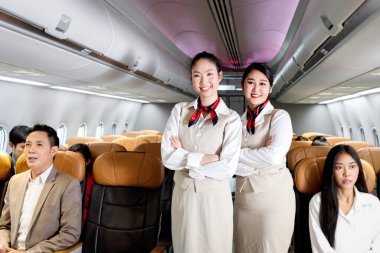 Asyalı iki güzel kadın hostesin portresi. Üniformalı. Uçakta kollarını kavuşturmuş duruyor..