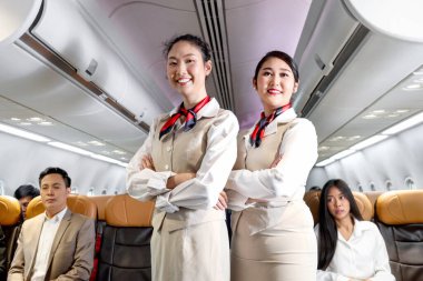 Asyalı iki güzel kadın hostesin portresi. Üniformalı. Uçakta kollarını kavuşturmuş duruyor..