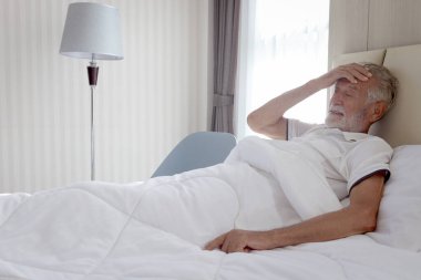 Erkek kıdemli hasta hastane yatağında yatıyor. Yaşlı bir adam kendini hasta hissediyor, evde dinlenme ihtiyacı duyuyor, hasta bir adamın başı ağrıyor, acı yüzünden elini alnına koyuyor. Yaşlılar sağlık hizmeti kavramı