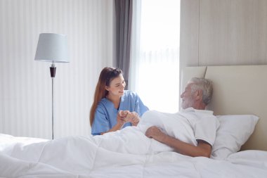 Hastane yatağında yatan erkek hastanın elini tutan güzel, şefkatli bayan doktor. Hemşire kendini hasta hisseden yaşlı bir adama bakıyor. Evde dinlenme ihtiyacı, sağlık hizmetleri...