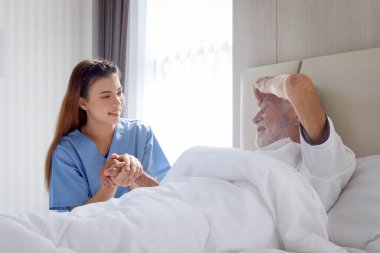 Hastane yatağında yatan erkek hastanın elini tutan güzel, şefkatli bayan doktor. Hemşire kendini hasta hisseden yaşlı bir adama bakıyor. Evde dinlenme ihtiyacı, sağlık hizmetleri...