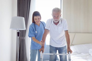 Kadın hemşire ya da doktor yaşlı bir adama ortopedik yürüyüşçüyle yürümesi için yardım ediyor, hasta muayenehanesinde fizyoterapist ile yürüyor, evde yaşlılara bakıcılık yapıyor, tıbbi bakım yapıyor..