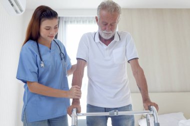 Kadın hemşire ya da doktor yaşlı bir adama ortopedik yürüyüşçüyle yürümesi için yardım ediyor, hasta muayenehanesinde fizyoterapist ile yürüyor, evde yaşlılara bakıcılık yapıyor, tıbbi bakım yapıyor..