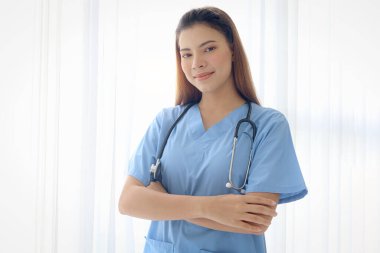 Steteskoplu mutlu gülümseyen güzel kadın doktor portresi klinik hastanesinde kolları çapraz duran mavi ceketli. Beyaz geçmişi olan kadın hemşire, sağlık çalışanı..