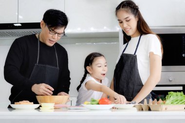 Mutfakta mutlu aile yemekleri, baba anne ve tatlı kız evde yemek yaparken eğleniyorlar. Ebeveynler ve çocuk yemek yapmayı, birlikte vakit geçirmeyi severler. Aile sevgisi ve bağlılık.