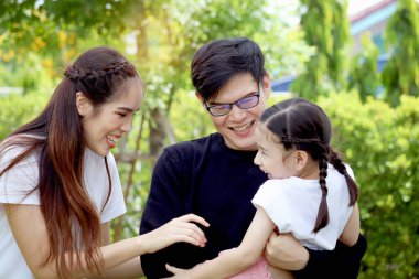 Mutlu bir aile yazın yeşil bahçede eğleniyor, anne ve baba çocukla oynuyor, baba tatlı kızı taşıyor, neşeli bir ebeveyn ve çocuk arka bahçede, aile bağlarını seviyor.