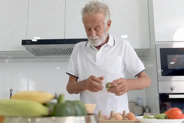 Elderly man standing at kitchen counter with colorful fresh vegetables, fruits and food ingredients, senior man preparing for cooking healthy food at home, mature grandfather making meal at kitchen.