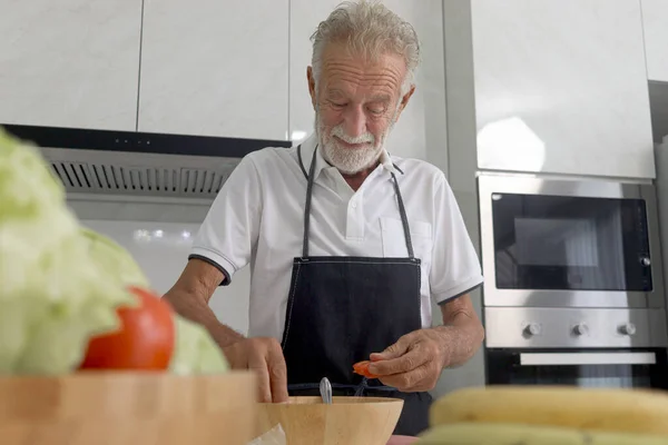 Elderly man standing at kitchen counter with colorful fresh vegetables, fruits and food ingredients, senior man preparing for cooking healthy food at home, mature grandfather making meal at kitchen.