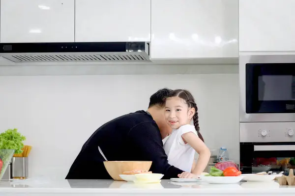 Happy family cooking at kitchen, father hugging cute daughter girl during having fun and making meal at home. Parent and kid child enjoy cooking food, spending time together. Family love and bonding.