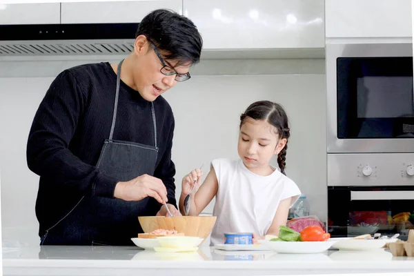 Happy family cooking at kitchen, father and cute daughter girl having fun during making meal at home. Parent and kid child enjoy cooking food and spending time together. Family love and bonding.