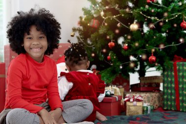 Afrikalı kız kardeş kış tatilini birlikte kutluyor. Kıvırcık saçlı tatlı kız kardeşi oturma odasındaki güzel Noel ağacının altında kardeşiyle oynuyor. Mutlu Noeller, mutlu çocukluk ailesi.