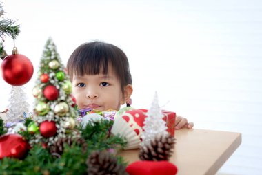 Küçük tatlı Asyalı kız çocuğu beyaz oturma odasında güzel bir Noel ağacını süsleyip süslüyor. Kış tatilini kutlayan çocuğa konsantre ol. Mutlu Noeller ve mutlu yıllar. Mutlu çocukluk