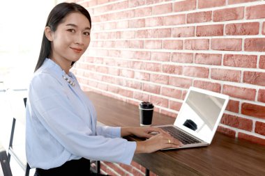 Mutlu gülümseyen Asyalı güzel bir kadının portresi turuncu tuğla duvarın yanında oturuyor. Kadın personel kafede dizüstü bilgisayarla çalışıyor. İş sırasında kahve içen memurlar, kahve dükkanında çalışan insanlar..