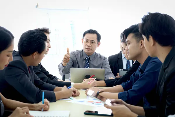 Businesspeople discussing at conference, happy senior businessman giving thumb up to admire compliment at group meeting. Elderly boss discussing with teammate, company teamwork brainstorming meeting.
