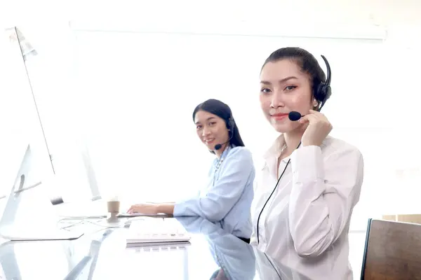 Portrait of happy smiling beautiful Asian woman with headphones work with computer at call center service desk, female agent with headsets talk with customer on hotline, operator with hands-free phone