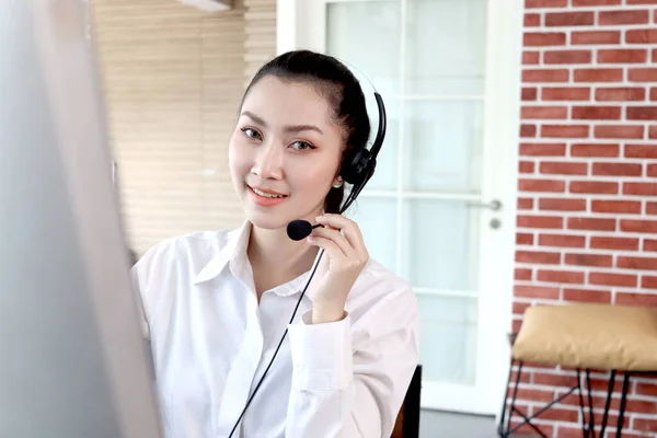 Portrait of happy smiling beautiful Asian woman with headphones work with computer at call center service desk, female agent with headsets talk with customer on hotline, operator with hands-free phone