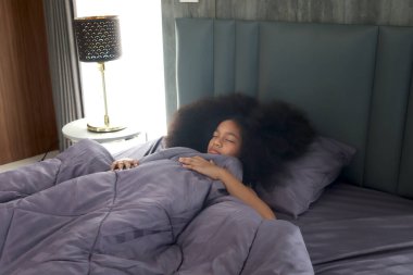 Afrikalı Asin melez, kıvırcık saçlı, yatak odasında rahat uyuyan kız çocuğu hafta sonu tatilinde geç kalkıyor. Tembel çocuk hala yatakta yatıyor..