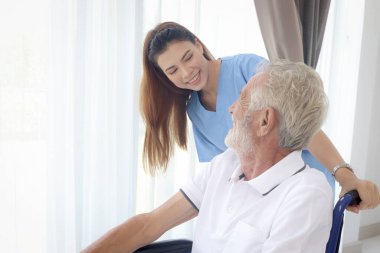 Evde tekerlekli sandalyedeki yaşlı hastayla ilgilenen güzel kadın hemşire tekerlekli sandalyede oturan engelli yaşlı adam, yetişkin büyükbabaya yardım eden genç kadın doktor, tıbbi bakım..