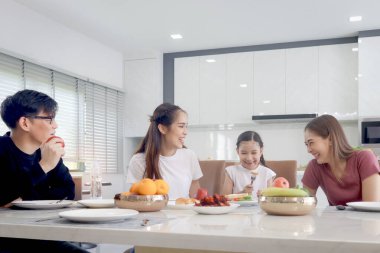 Mutlu bir aile yemek odasında yemek yiyor. Ebeveynler, kız ve halalar yemek masasında oturup kahvaltıda eğleniyorlar. Neşeli aile, anne baba ve çocuk birlikte yemek yemekten hoşlanırlar..