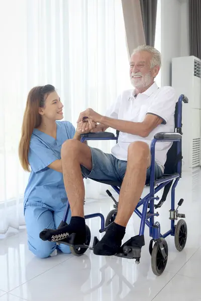 Happy senior patient in wheelchair with beautiful female nurse taking care of him at home, disabled elderly man sits in wheelchair, woman doctor helping mature grandfather, nursing medical health care