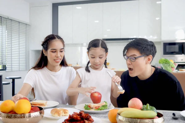 Happy family has meal in dining room. Parents, mother father and kid daughter sit at dining table and have fun during breakfast or lunch. Cheerful family enjoy eating food and spending time together.