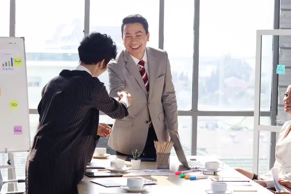 Successful senior Asian businessman shares experience success, gives presentation, shaking hands with businesswoman at conference meeting desk, businesspeople have discussion in office workplace.