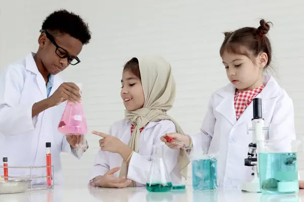 Three little cute girls and African boy in lab coat do science experiment together, diversity group student of young scientist kid have fun in chemistry laboratory, children do research at school.