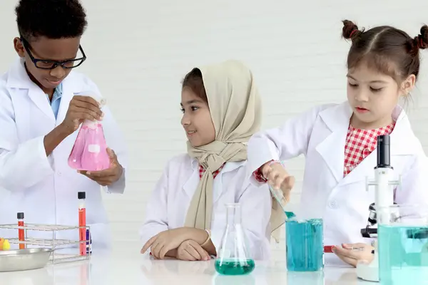 Three little cute girls and African boy in lab coat do science experiment together, diversity group student of young scientist kid have fun in chemistry laboratory, children do research at school.