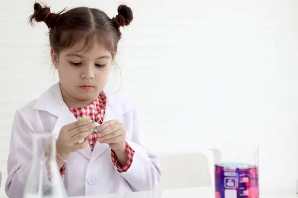 Cute little girl in lab coat doing science experiment at class room, young schoolgirl scientist kid having fun in chemistry laboratory class, little children doing research at school.