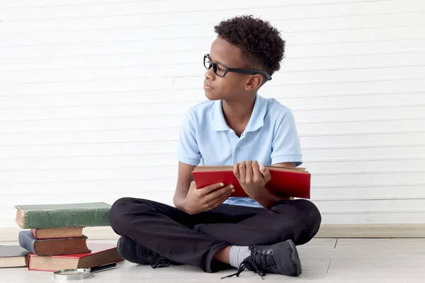 真剣に濃縮されたアフリカの少年は白い壁の部屋の本の積み重ねで床に座っている間に眼鏡をかけている 子供の教育 発見を探求するかわいい子供 ロイヤリティフリーのストック写真