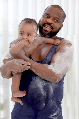 Mutlu Afrikalı bir aile, banyo yaptıktan sonra bebek bebek kucağında babalar ve banyo hazır vücut pudrasına talk pudrası sürerler. Baba ailenin küçük tatlı kızına bakıyor..