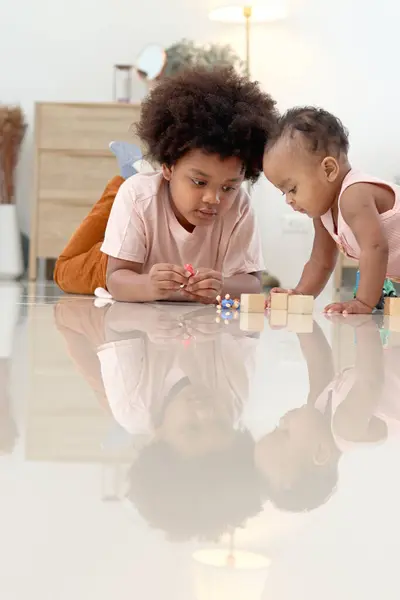 Happy African family spending time together, brother boy with black curly hair lying on floor, playing toy with little cute toddle baby infant kid in bedroom. Sibling relationships in childhood.