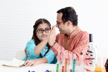 Geleneksel giysili şirin Hintli kız babası veya öğretmeniyle laboratuarda fen deneyleri yaparken beş el hareketi yapıyor. Laboratuvar ekipmanlı bilim adamı çocuk kimya sınıfını öğreniyor.