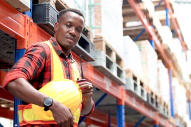 Güvenlik yeleği giyen genç Afrikalı bir adamın portresi. Kaskı ve telsizi var. Depo fabrikasında duruyor. Mele kargo lojistik personeli nakliye deposunda çalışıyor..