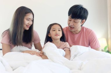 Mutlu Asyalı aile yatak odasında eğleniyor. Baba ve anne kız, beyaz yatakta yatarken vücudu battaniyeyle örterler. Ebeveynlerin ve küçük kız çocuklarının evde iyi bir hafızaları var. Ebeveynlik ve çocukluk